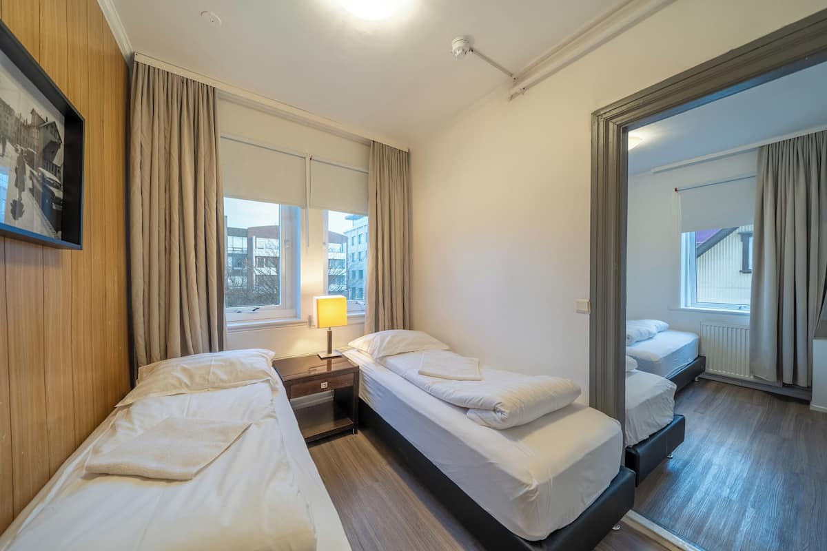 Hotellihuone, jossa on kaksi erillistä sänkyä, yöpöytä lampun kanssa, ikkuna, jossa on verhot, ja peili, joka heijastaa huonetta.