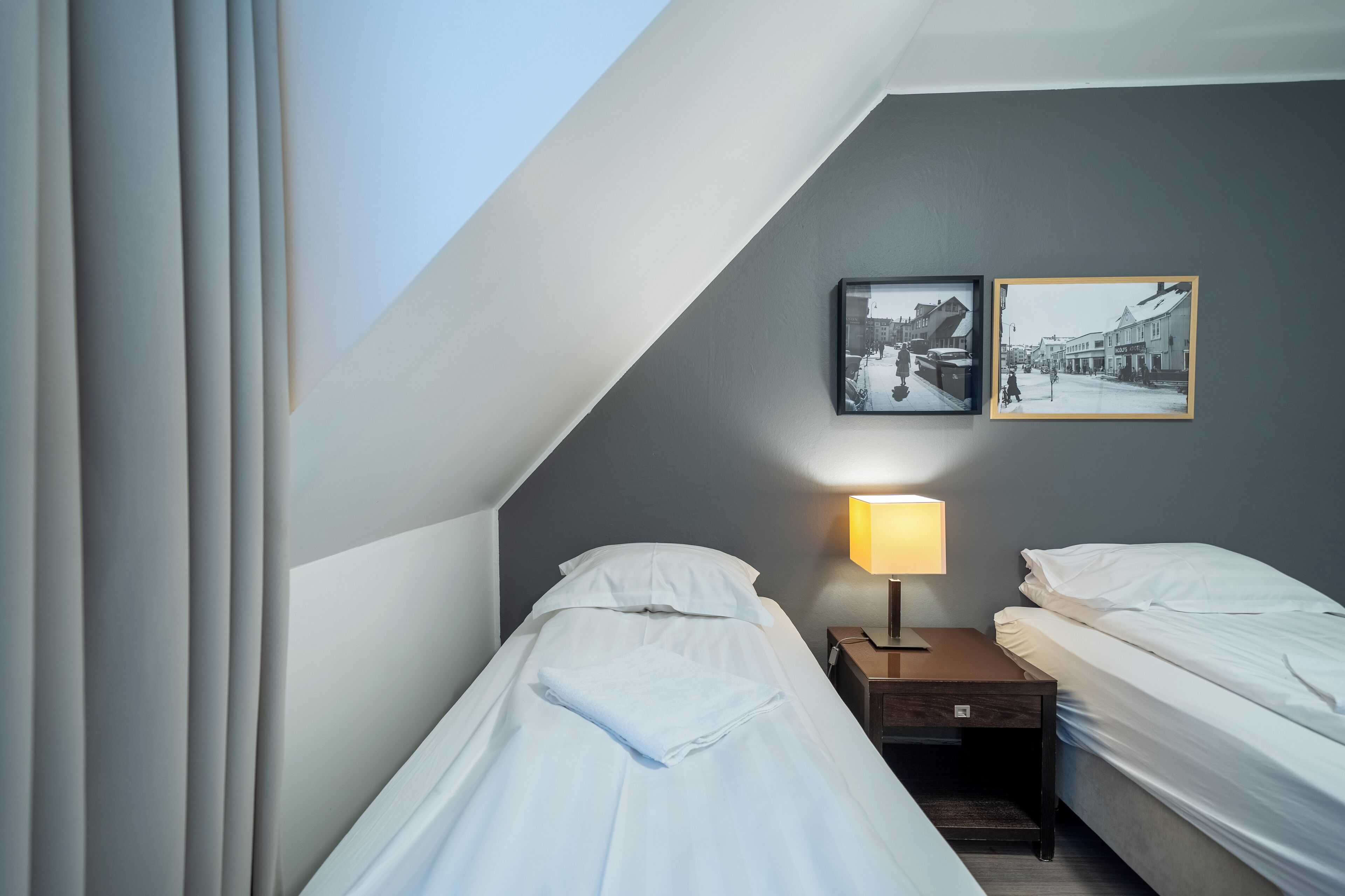 Una habitación de hotel con dos camas individuales, una mesita de noche con lámpara y dos cuadros enmarcados en la pared.