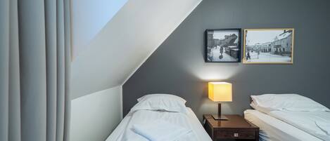 Una habitación de hotel con dos camas individuales, una mesita de noche con lámpara y dos cuadros enmarcados en la pared.