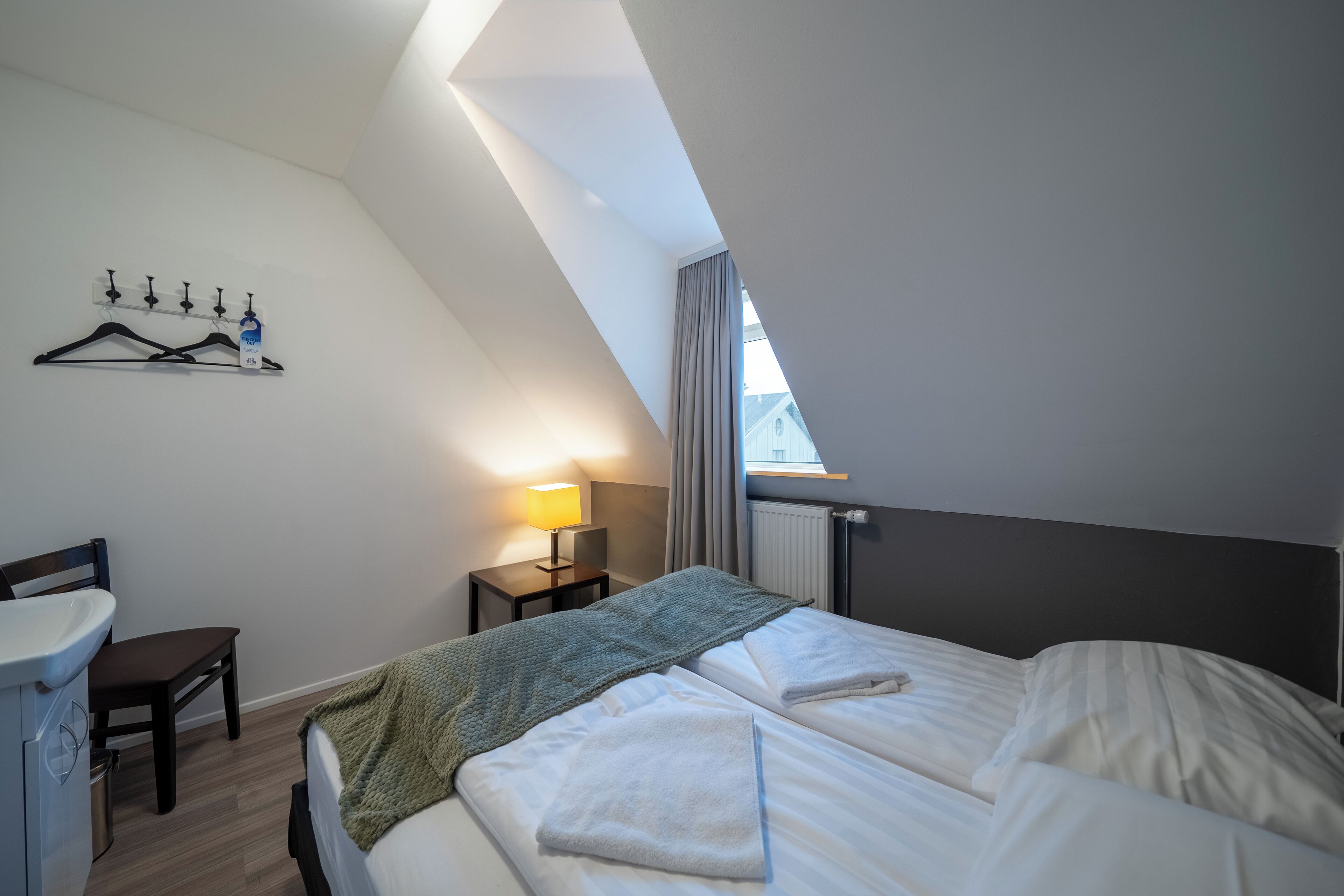 Quarto com cama, escrivaninha, cadeira, radiador e janela com cortinas.