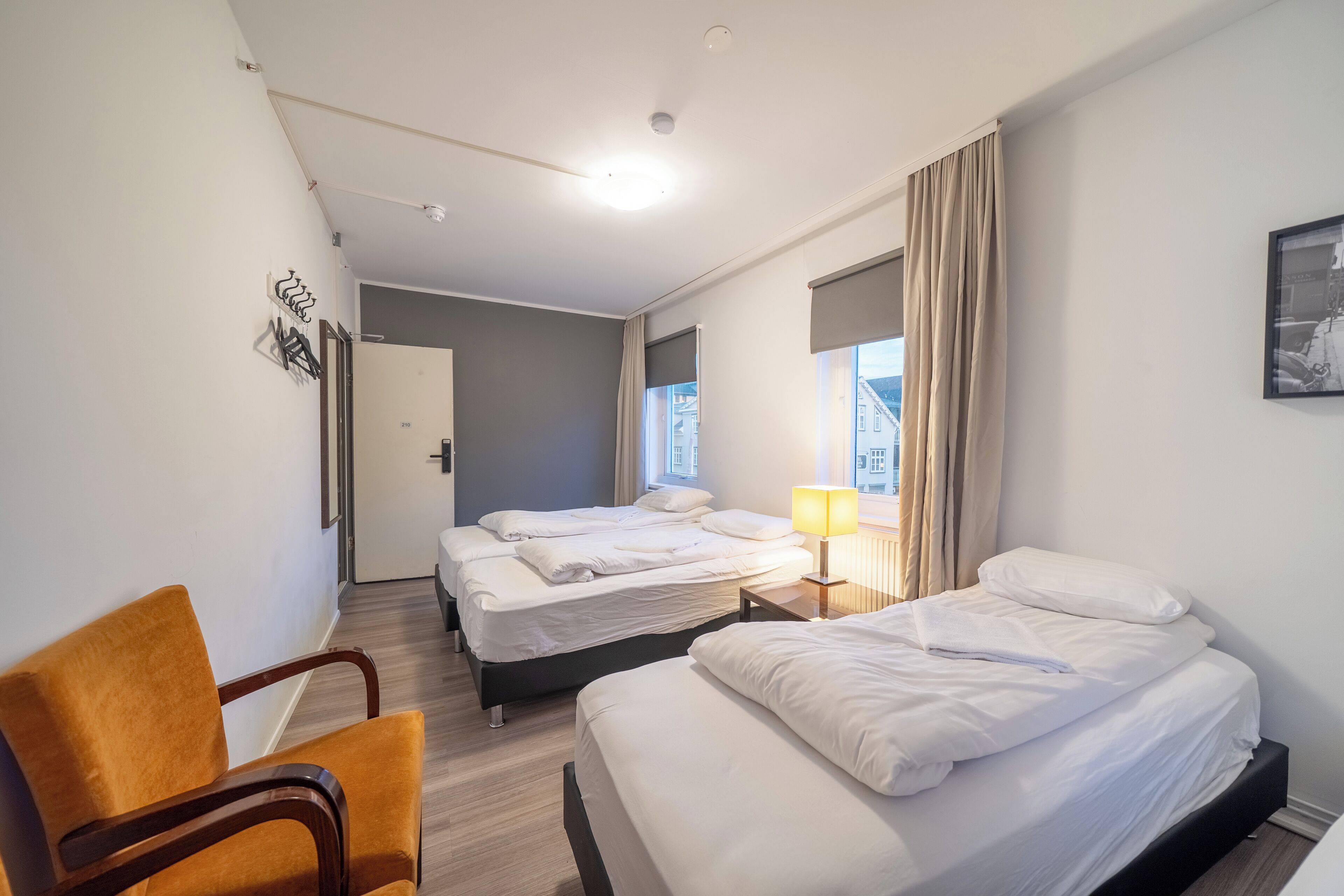 A hotel room with two beds, a chair, a lamp, and a door leading to another room.