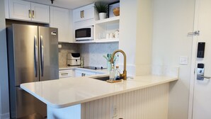 Une cuisine moderne avec des meubles blancs, des appareils en acier inoxydable, un îlot central doté de tabourets et un micro-ondes encastré.