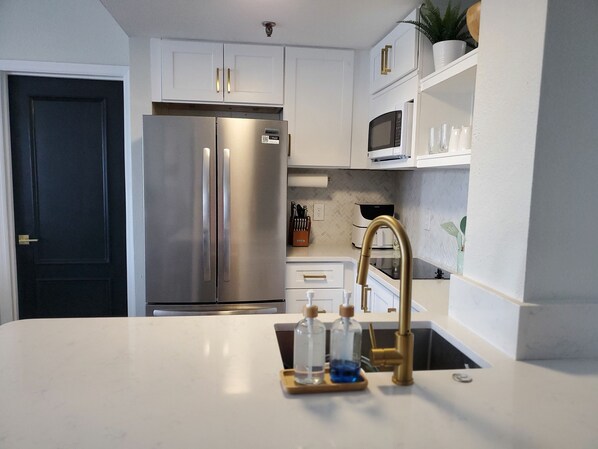 A modern kitchen with white cabinets, stainless steel appliances, and a marble countertop. - 2 BD/2 BA minutes from Universal Studios & Epic Universe (Orlando)