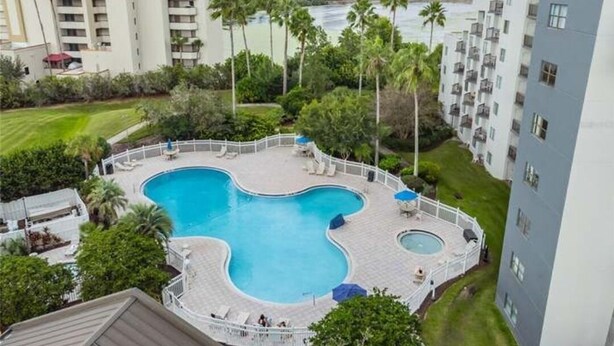 Une piscine à la forme originale, entourée d’une terrasse blanche, de palmiers et, en arrière-plan, d’un paysage urbain.