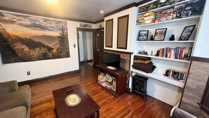 A living room with a wooden floor, a fireplace, a bookshelf, and a large painting of a mountain landscape. - Launch your next adventure from here: plenty of beds, plenty of parking, plenty of fun (Plymouth)