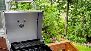 A Char-Broil gas grill with a stainless steel finish, two control knobs, and a side burner, set on a wooden deck with a garden background. - Launch your next adventure from here: plenty of beds, plenty of parking, plenty of fun (Plymouth)