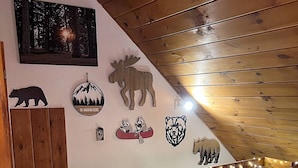 Een gezellige kamer met een schuine balken plafond, houten wanden en een bed met beddengoed met een patroon. Er staat een stoel in de hoek en een klein tafeltje bij het bed.