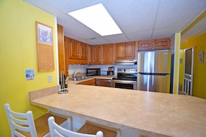 A kitchen with wooden cabinets, a stainless steel refrigerator, a microwave, and a stove.