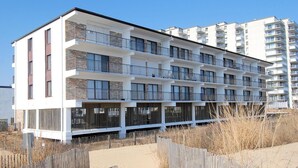 A multi-story residential building with balconies, a sandy pathway, and a wooden fence.