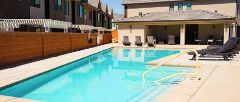 A swimming pool with lounge chairs and a covered seating area.