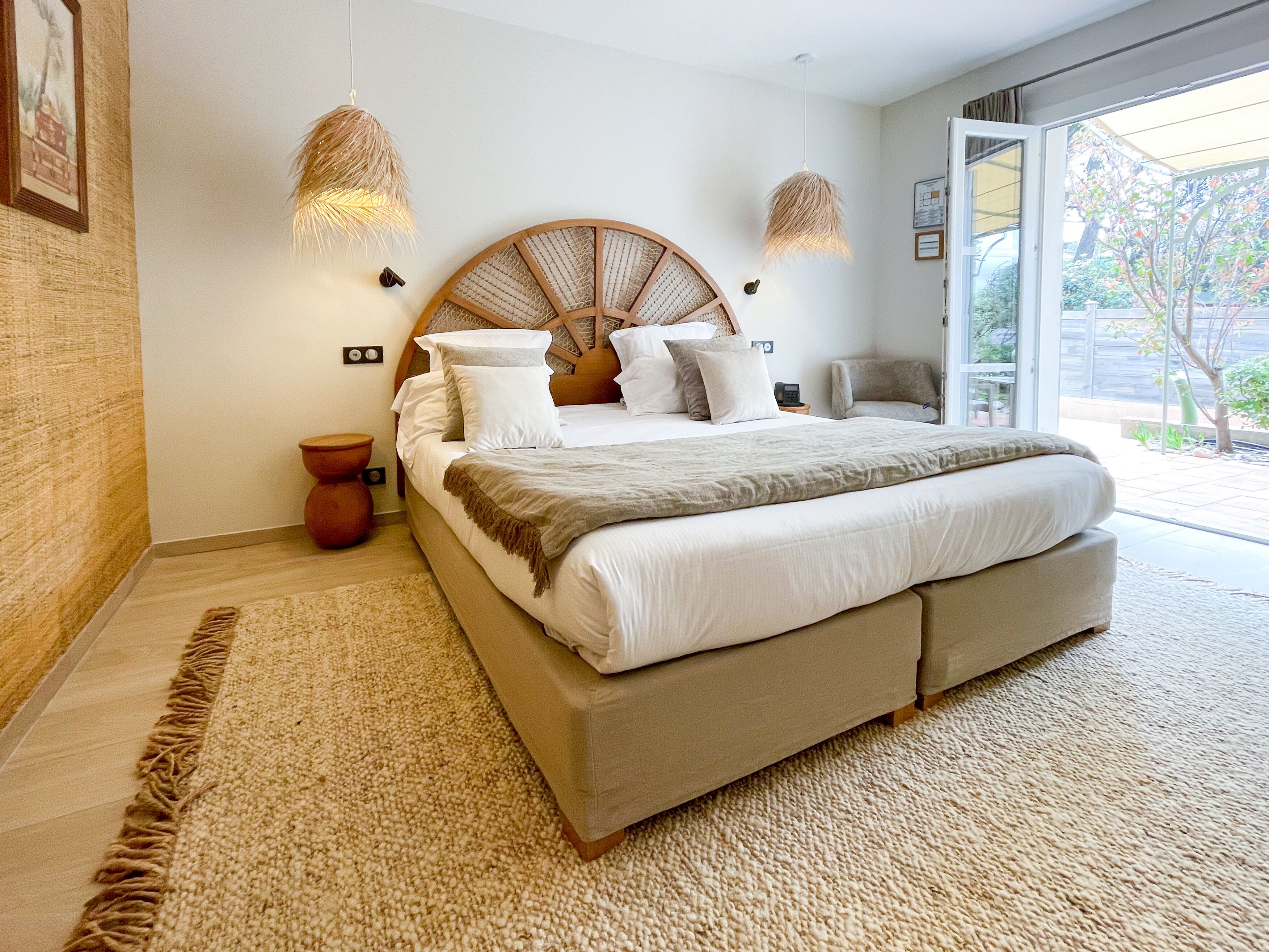 A large bed with a wooden headboard, two bedside lamps, and a view of the outdoors through a sliding glass door.