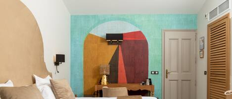 Una habitación de hotel con cama, escritorio, silla, un cuadro en la pared y una puerta.