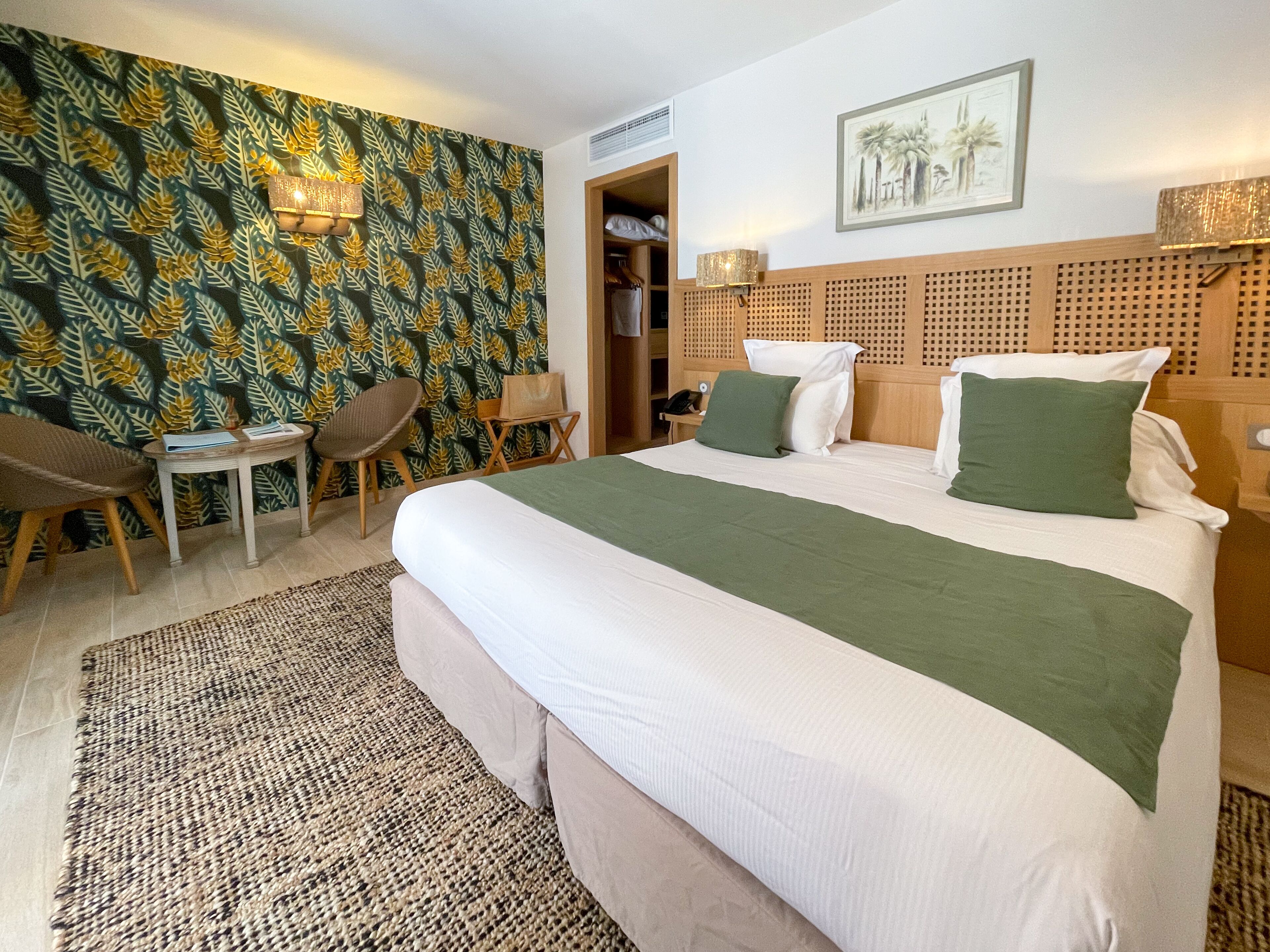 A hotel room with a bed, a desk, a chair, a wardrobe, and a patterned wallpaper.
