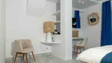 A modern bedroom with a bed, a chair, a desk, and a vanity with a mirror.