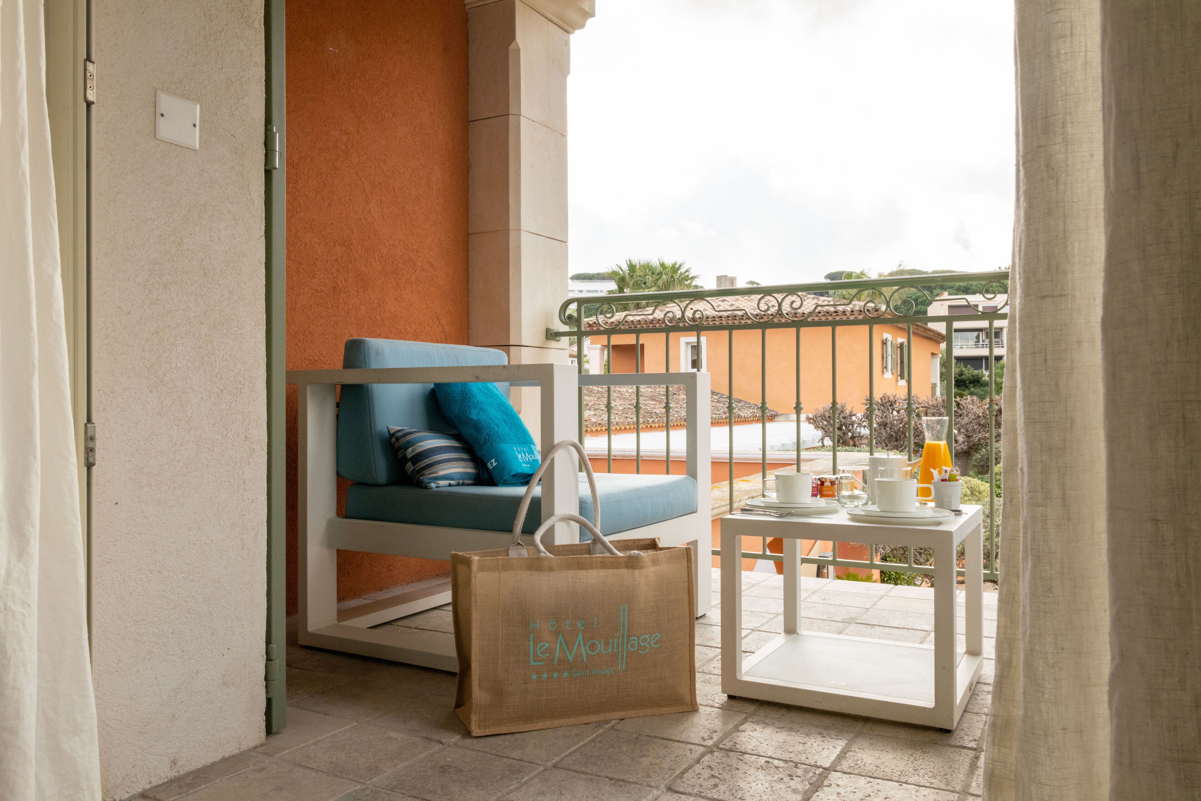 A balcony with a blue chair, a white table with a tray, and a brown bag with text.