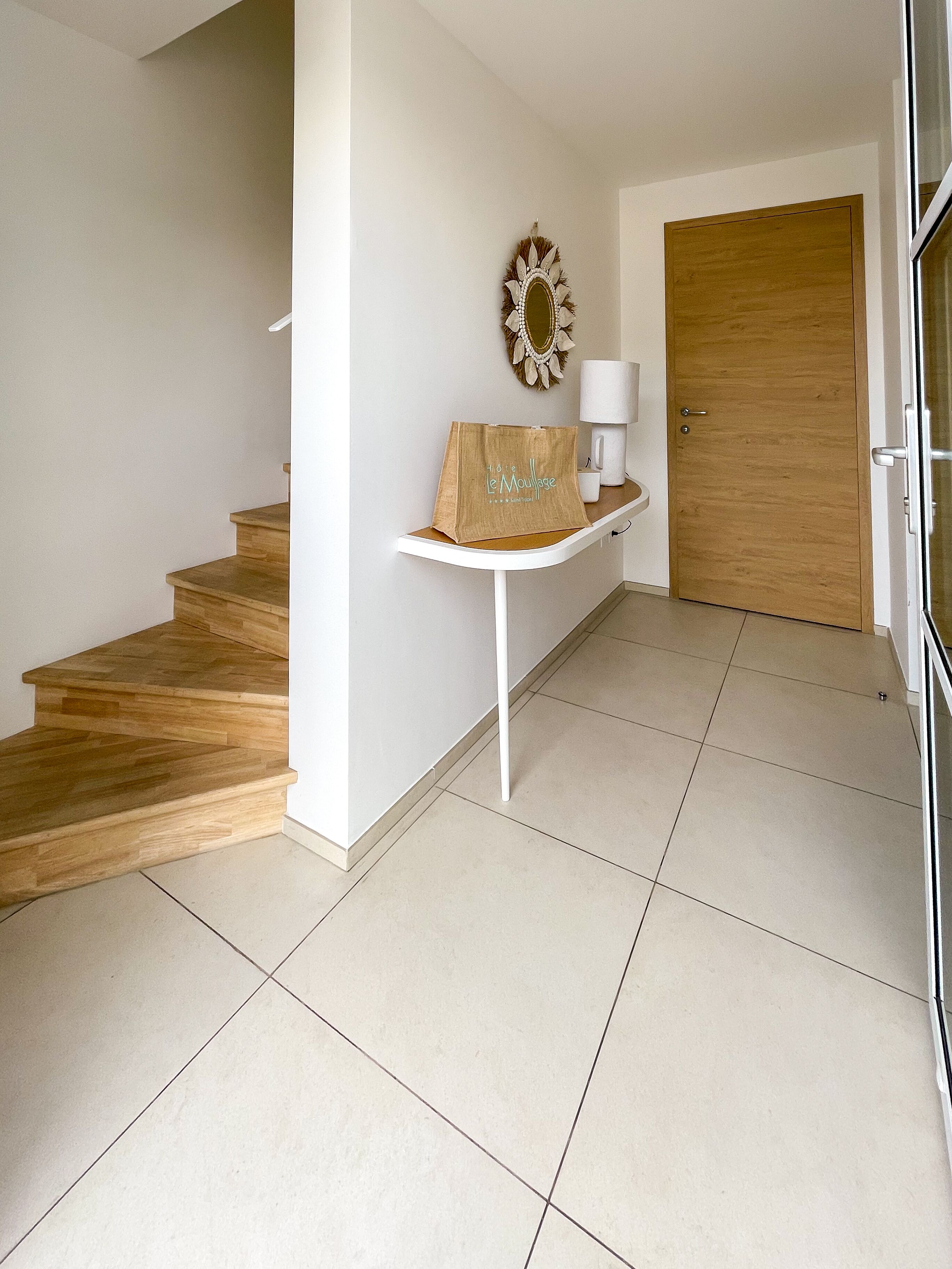Een net, modern interieur met een houten trap, een witte console tafel met een decoratieve spiegel en een houten deur.