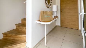Een net, modern interieur met een houten trap, een witte console tafel met een decoratieve spiegel en een houten deur.