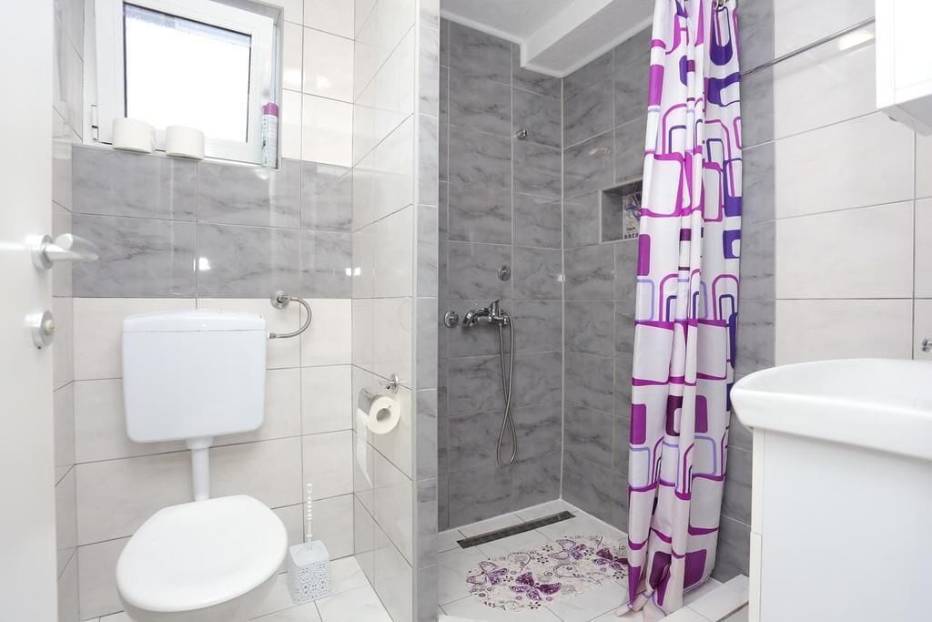 A bathroom with a toilet, shower, and a window above the toilet.