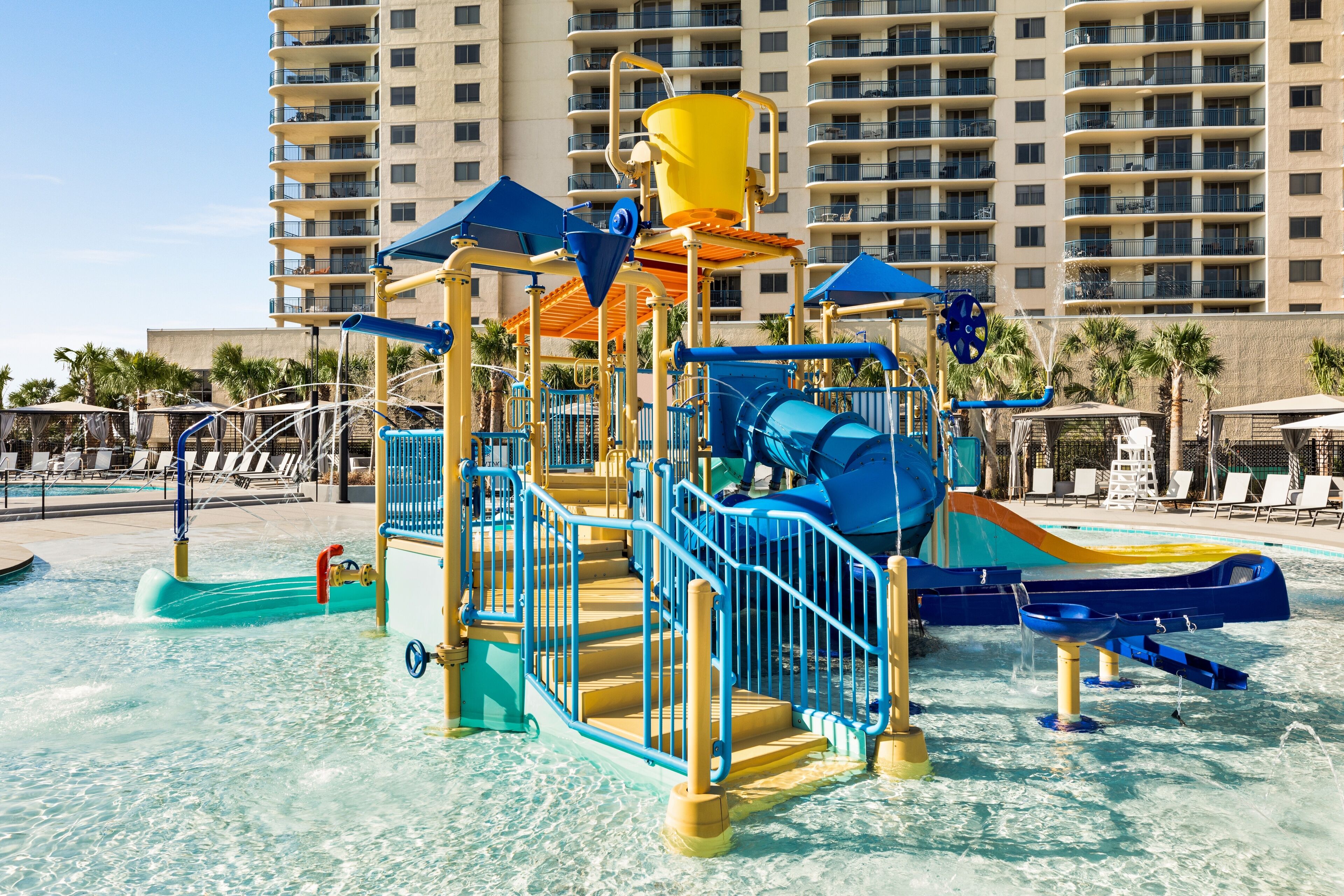 A water park with slides and play structures, surrounded by a pool and lounge chairs.