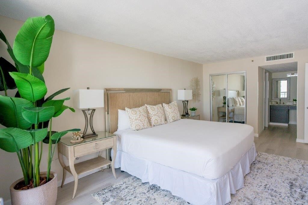 Une chambre à coucher avec un grand lit, des tables de chevet, une commode, un miroir et une plante en pot.
