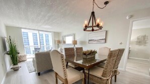 Comedor con mesa de madera y sillas de mimbre, un candelabro y vistas de la ciudad a través de amplios ventanales.