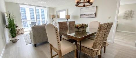 A dining area with a wooden table and wicker chairs, a chandelier, and a view of the city through large windows.