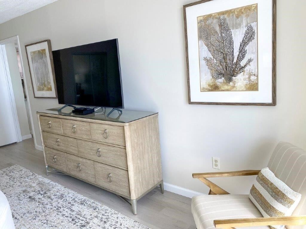 A modern living room with a flat-screen TV on a wooden cabinet, a white sofa, and two framed artworks on the wall.