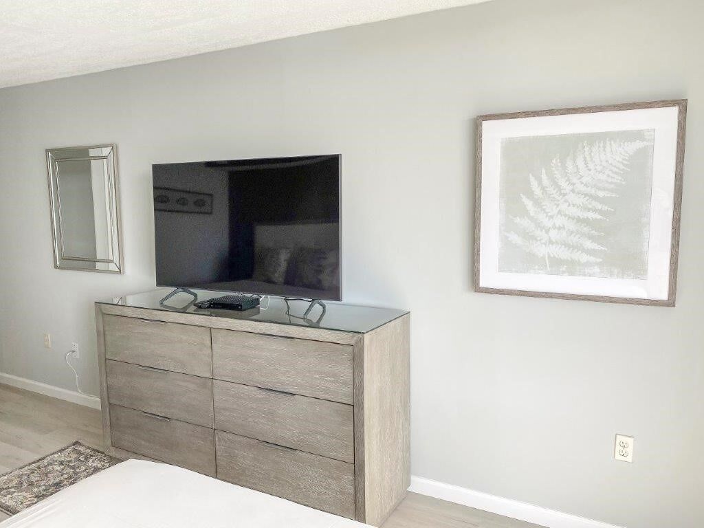 A bedroom with a dresser, a mirror, and a framed fern artwork on the wall.