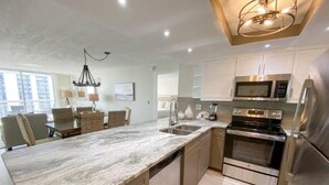 Una cocina moderna con encimera de mármol, electrodomésticos de acero inoxidable y comedor con mobiliario de mimbre.
