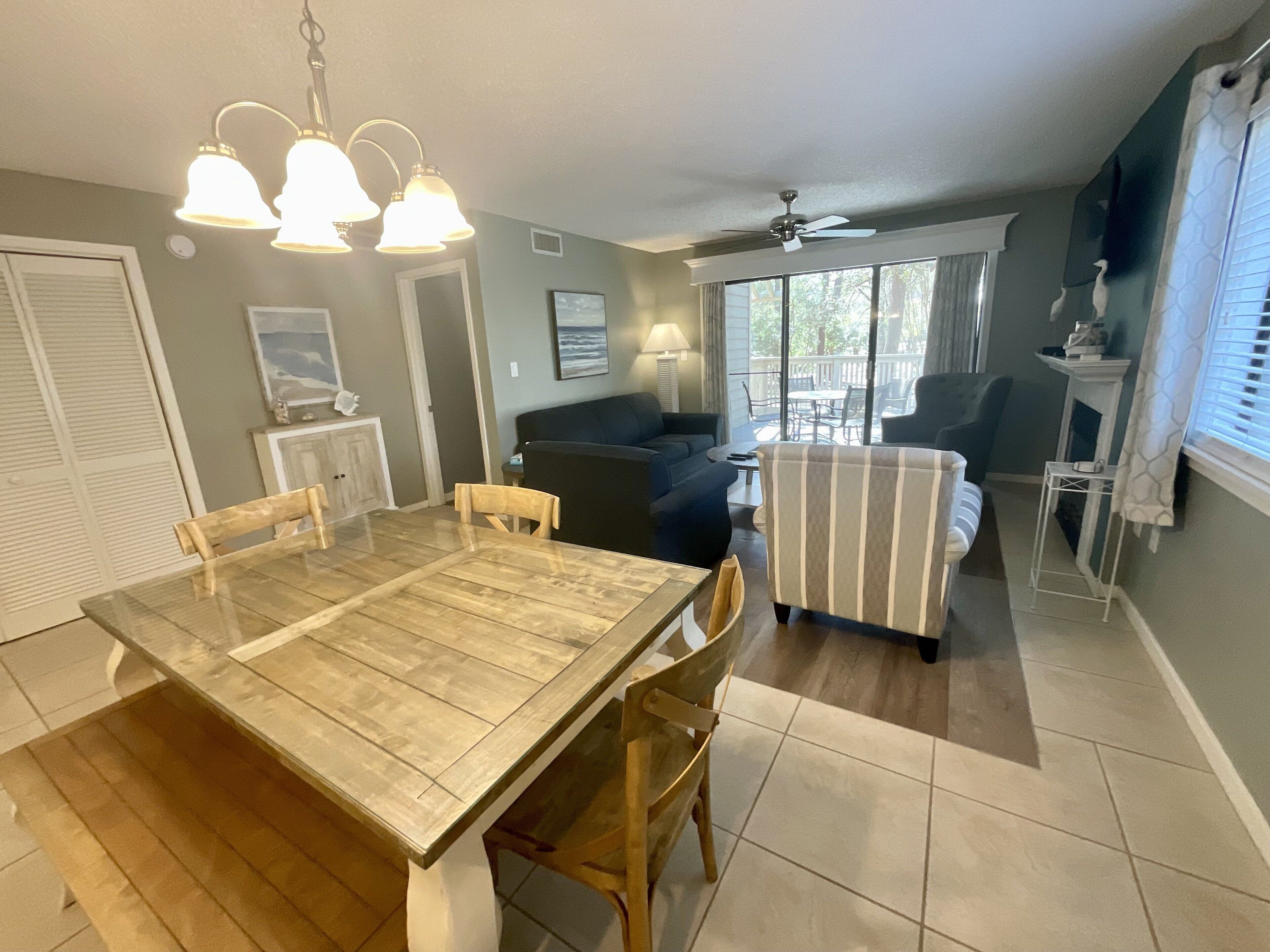 A dining area with a wooden table and chairs, a ceiling fan, and a view to the outside.