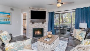 A living room with a stone fireplace, a flat-screen TV, and a large window with curtains. - Completely Remodeled And Open 18c Richmond Park 2 Bedroom Villa (Myrtle Beach)
