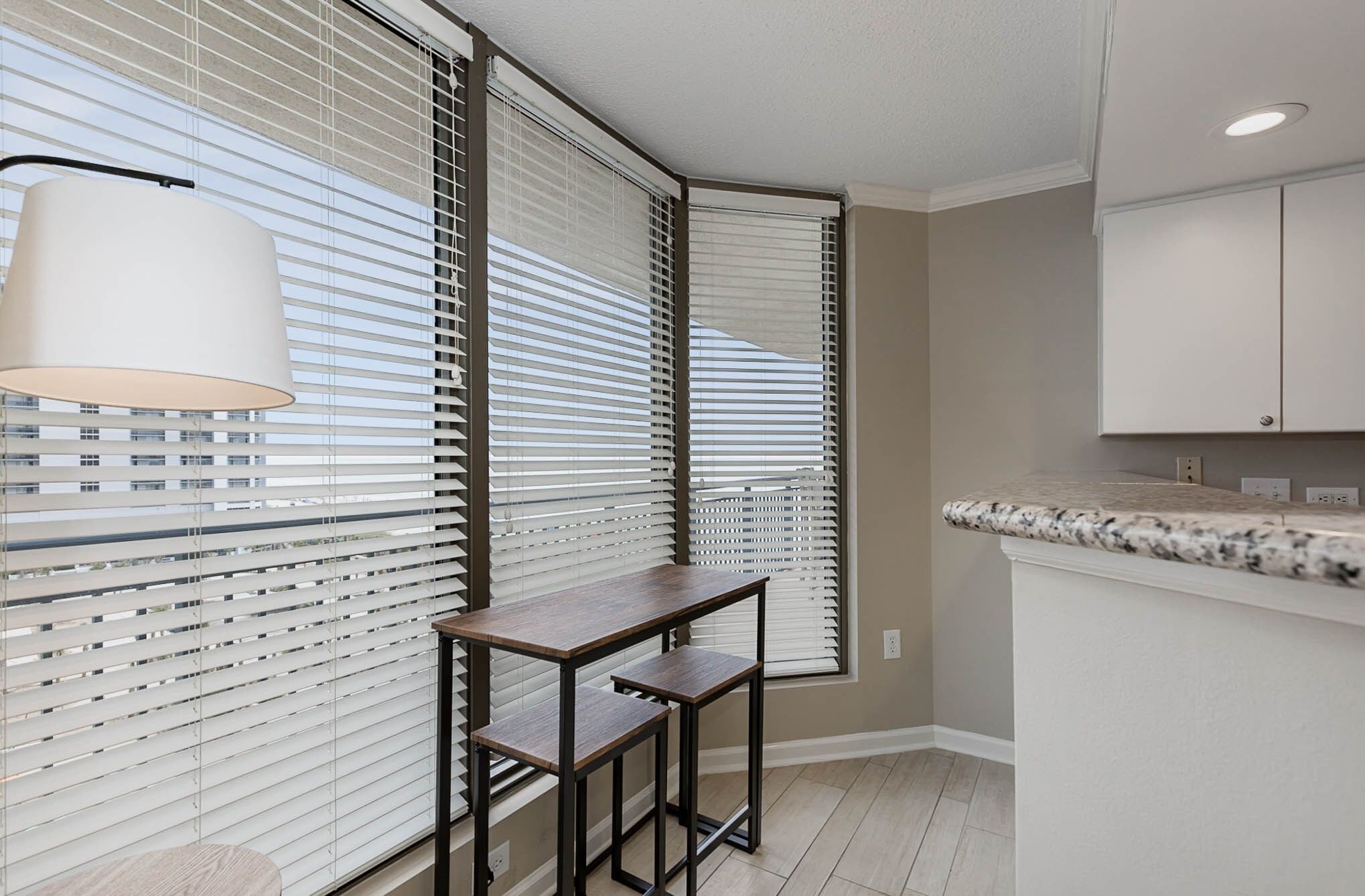 A kitchen with white cabinets, a marble countertop, and a window with blinds.