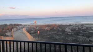 A beach view from a balcony with a wooden railing, sandy path, and sparse vegetation. - Bimini 107 2 Bedroom Condo by RedAwning (Ocean City)