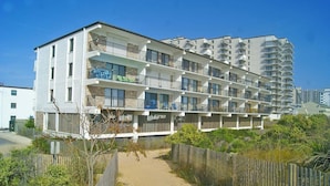 A multi-story hotel with balconies, a sandy pathway, and a wooden fence. - Bimini 107 2 Bedroom Condo by RedAwning (Ocean City)