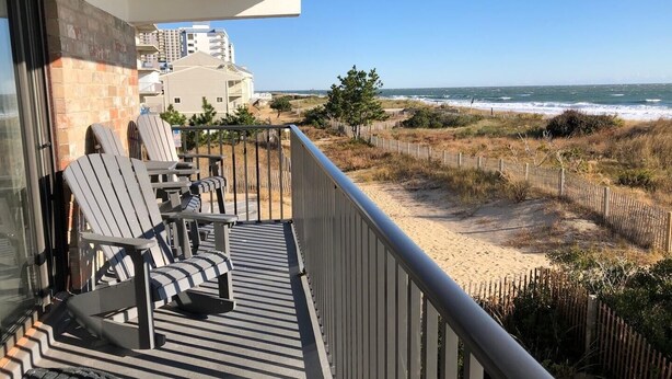 A balcony with two Adirondack chairs, a small table, and a view of the beach and ocean. - Bimini 107 2 Bedroom Condo by RedAwning (Ocean City)