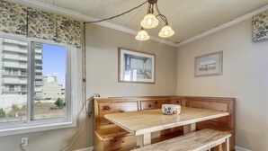 A corner room with a wooden bench, a table, and a window with a view of buildings. - Bimini 107 2 Bedroom Condo by RedAwning (Ocean City)
