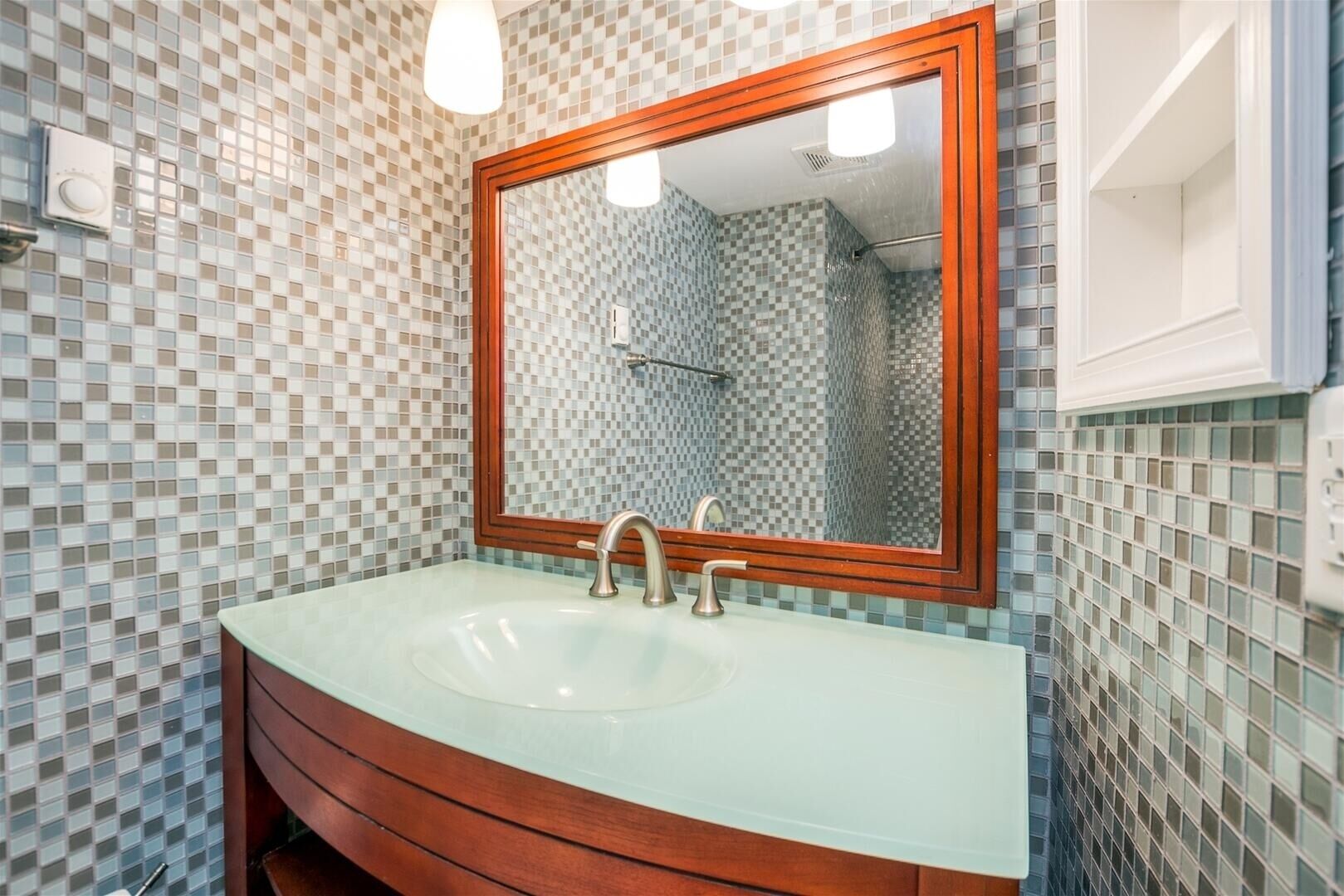 Een badkamer met een glazen wastafel, een houten opbergmeubel en wandtegels met mozaïek.