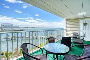 Uma varanda com cadeiras de vime e uma mesa, com vista para uma orla com cais e um edifício branco ao longe.