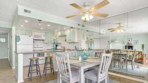 A modern kitchen with a central island, bar stools, and a dining area with a table and chairs.