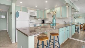 A kitchen with teal cabinets, a granite countertop, a white refrigerator, a microwave, a stove, and a vase with flowers on the island.