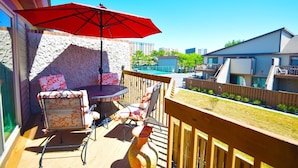 A wooden deck with a round table and chairs, a red umbrella, and a stone wall. - Club Ocean Villas Ii 19 2 Bedroom Condo by RedAwning (Ocean City)