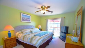 A bedroom with a bed, two bedside tables, a ceiling fan, a TV, and a balcony with a view. - Club Ocean Villas Ii 19 2 Bedroom Condo by RedAwning (Ocean City)