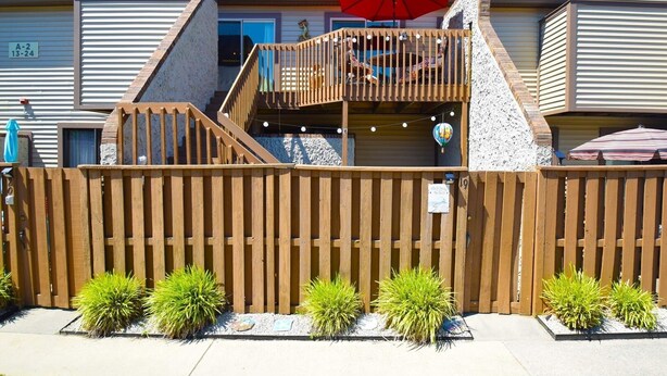 A two-story building with a wooden deck, a red umbrella, and a sign indicating a rental price of $19 per night. - Club Ocean Villas Ii 19 2 Bedroom Condo by RedAwning (Ocean City)