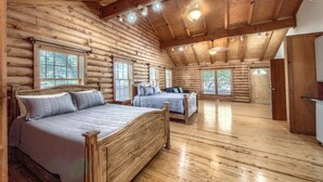 A log cabin bedroom with two beds, wooden floors, and a sloped ceiling with recessed lighting.