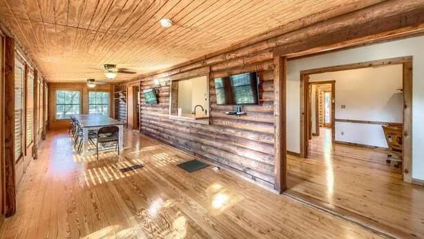 A log cabin interior with a dining area, a kitchen, and a TV mounted on the wall.