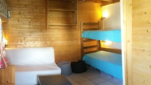 A cozy cabin interior with a wooden wall, a white sofa, a bunk bed with blue bedding, a small table, and a grey bean bag. - Apartment at Chalet Le Cordé in Beaufort, Savoie. Dominant view (Beaufort)