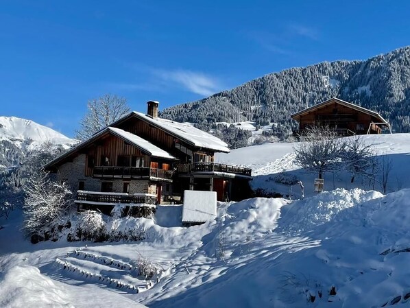 Una cabaña de madera con balcón, rodeada de colinas y árboles cubiertos de nieve.