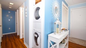 Une buanderie équipée d’un lave-linge et d’un sèche-linge, une console blanche surmontée d’une lanterne, et un mur bleu décoré d’étoiles.