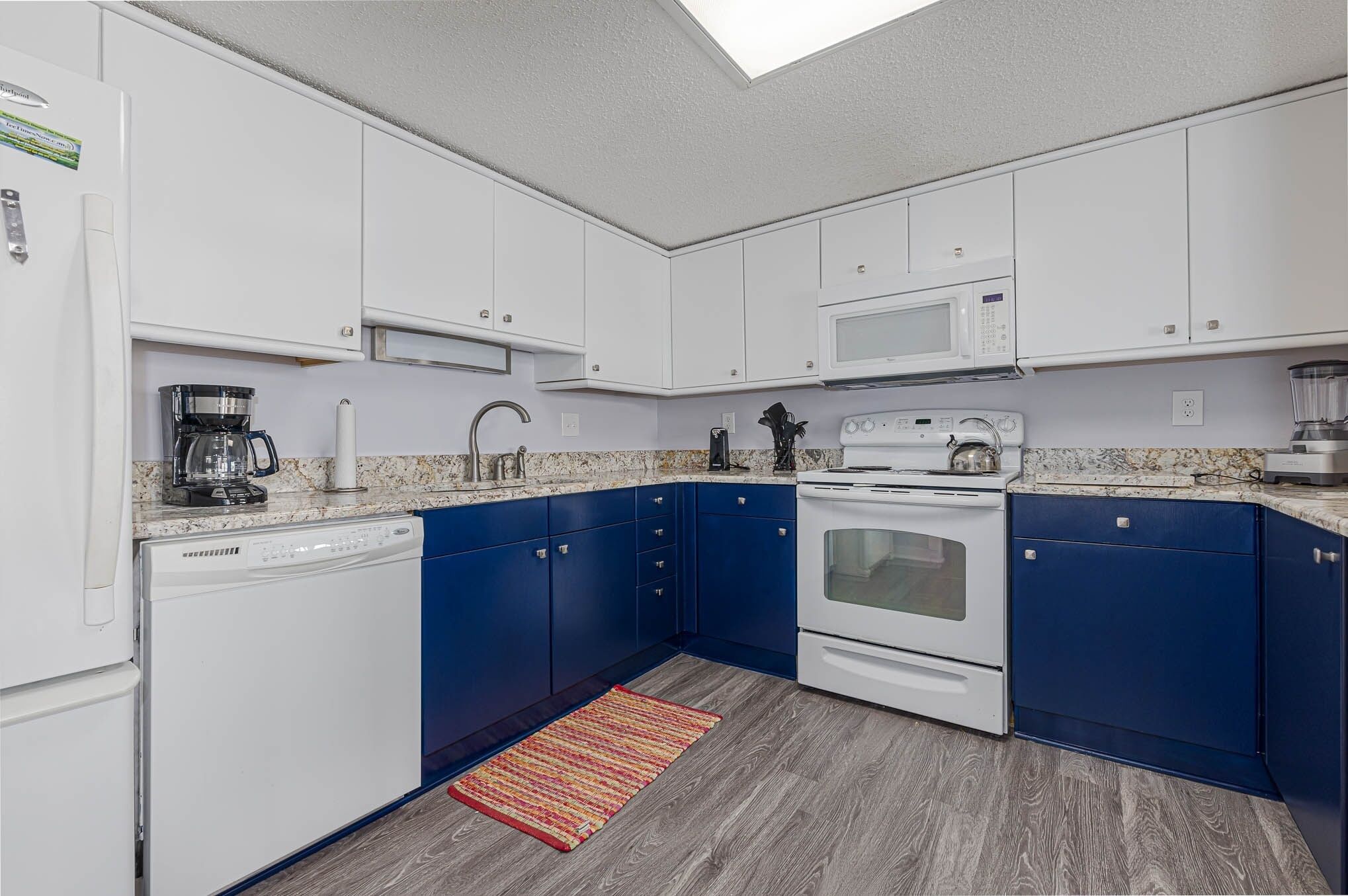 A compact kitchen with white and blue cabinets, a microwave, a coffee maker, and a dishwasher.