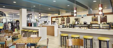 A café with multiple seating options including tables and bar stools, a counter with a menu, and a visible restroom area.